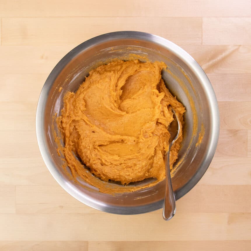 thick light orange muffin batter with metal mixing spoon on same bowl