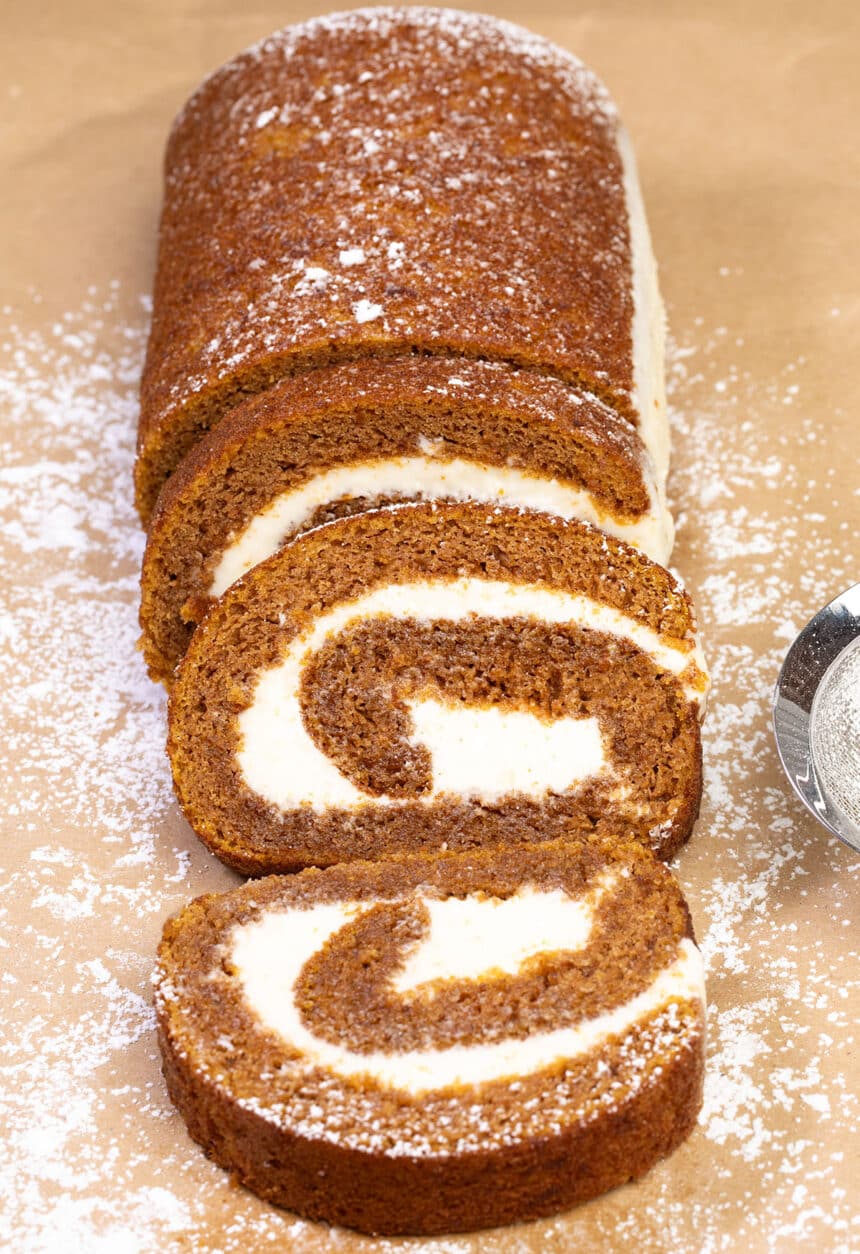 swirled orange cake roll with white filling on brown paper with powdered sugar sprinkled