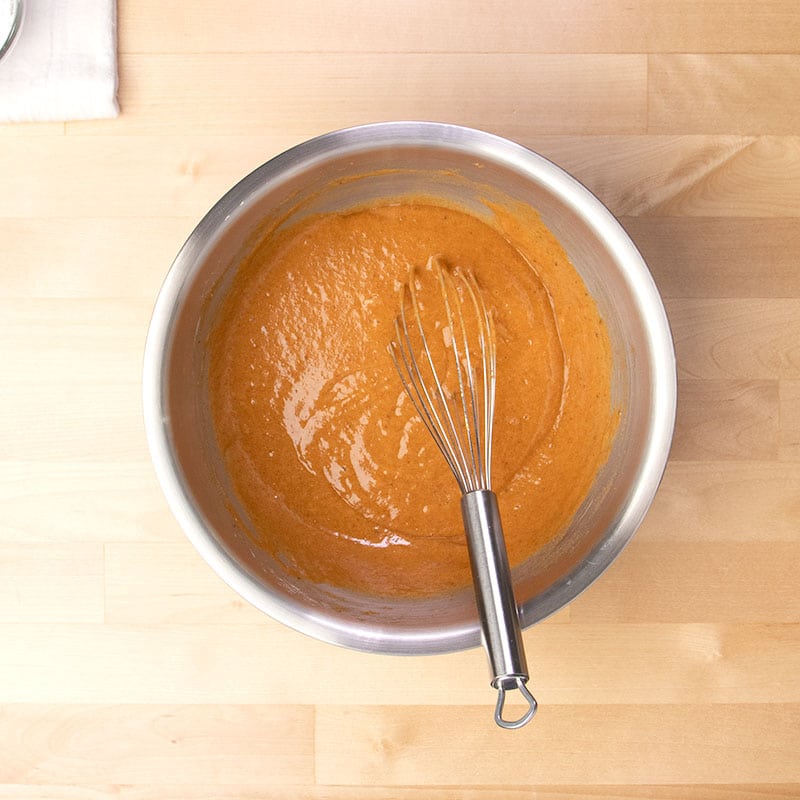 orange gluten free pumpkin roll batter with large metal whisk in same mixing bowl