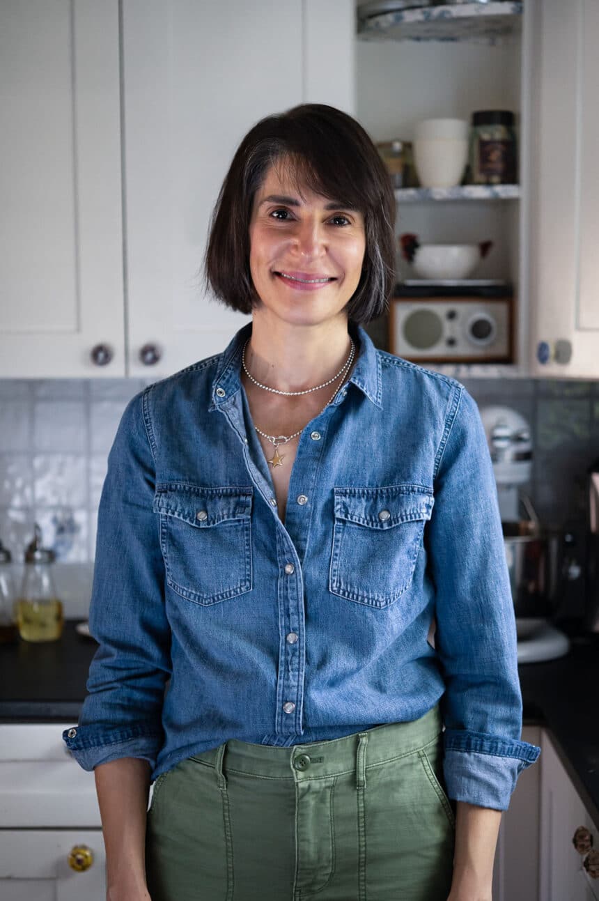 Nicole Hunn wearing blue denim shirt and green pants in kitchen with white cabinets