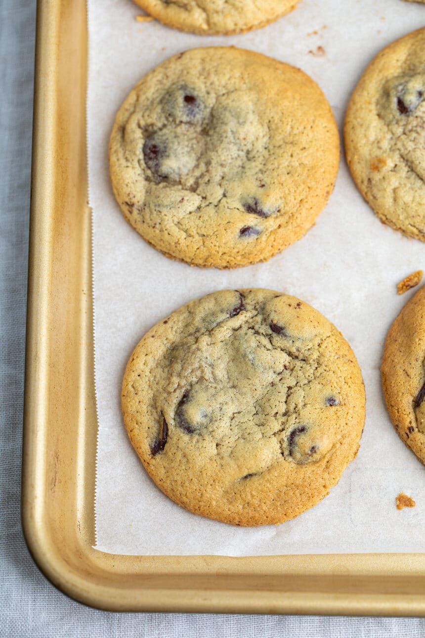 overhead closeup image of light brown cookies with chocolate chips baked on white paper lined gold baking tray