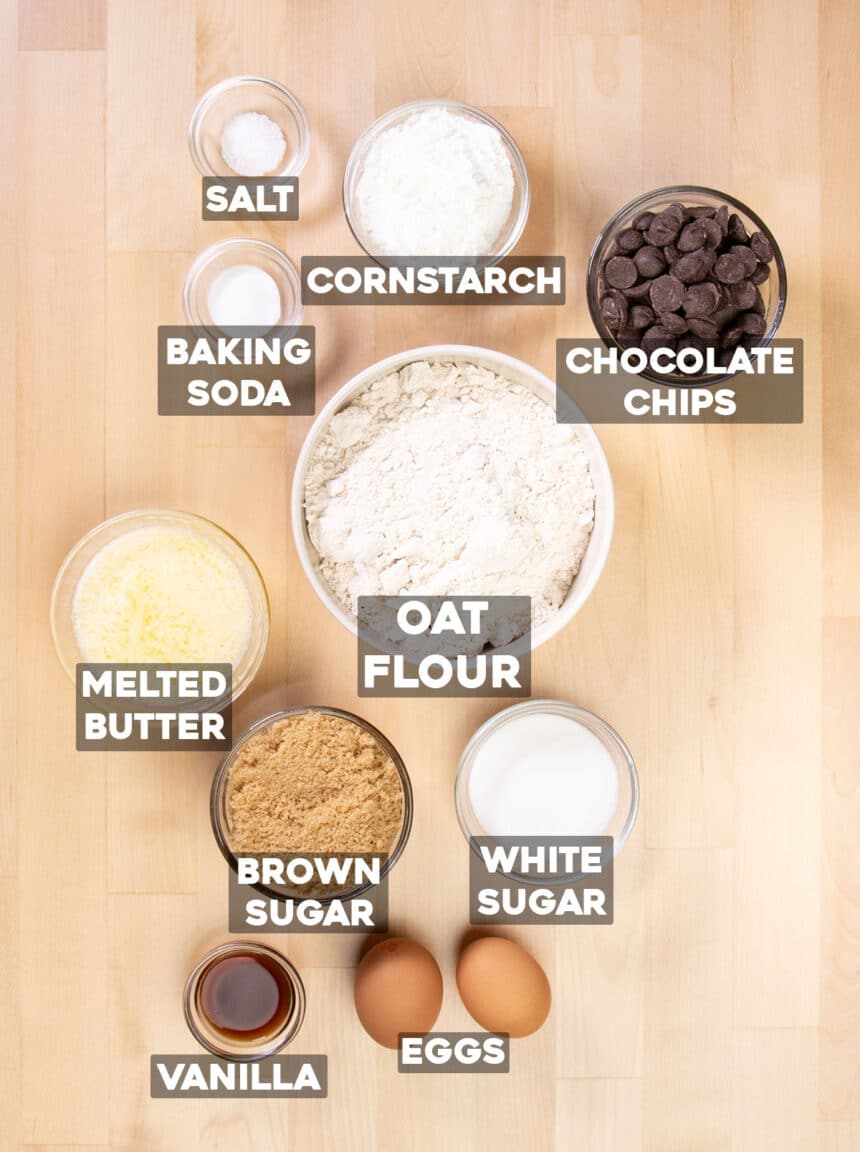 oat flour chocolate chip cookies ingredients in small bowls on light wood table with words of ingredients written on top