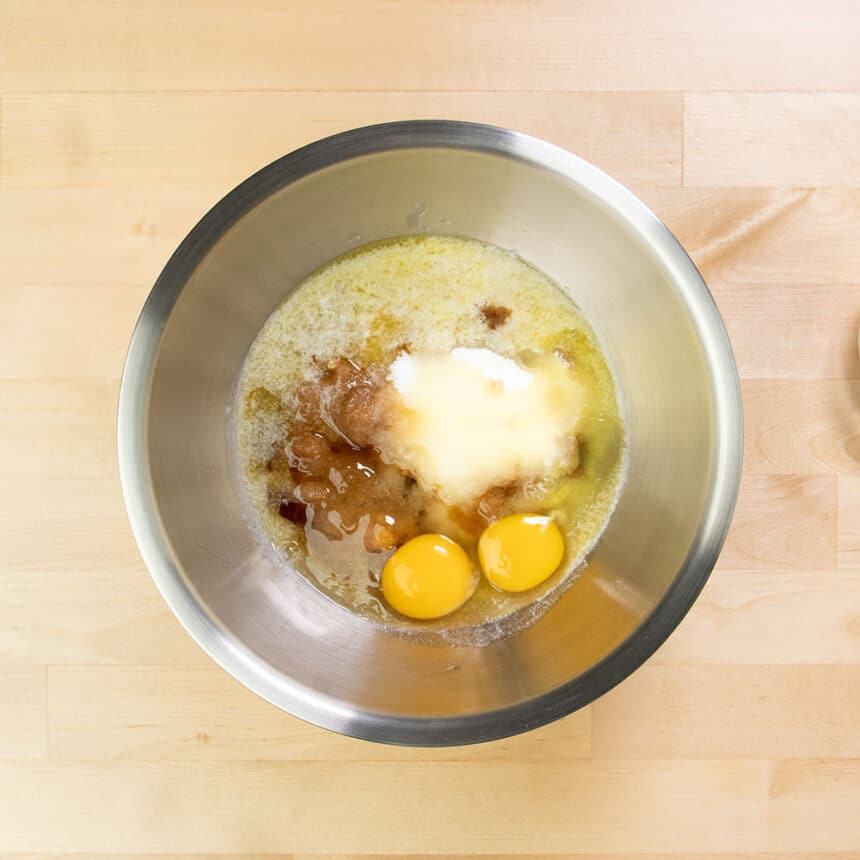 round metal mixing bowl with sugars, 2 raw eggs and melted butter