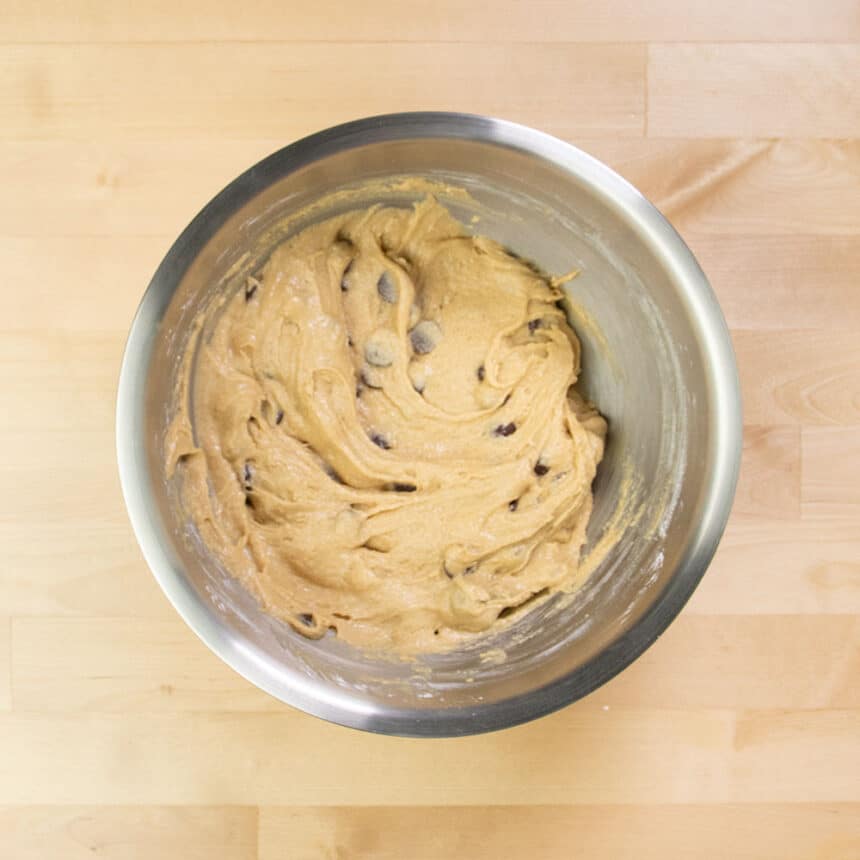 chocolate chips mixed in to light brown cookie dough in mixing bowl