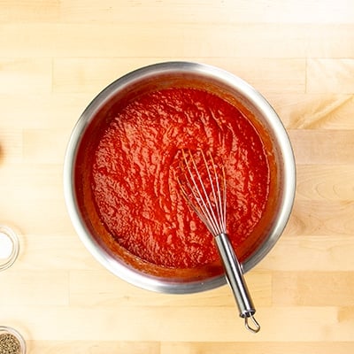 Red tomato sauce in large round metal bowl with whisk