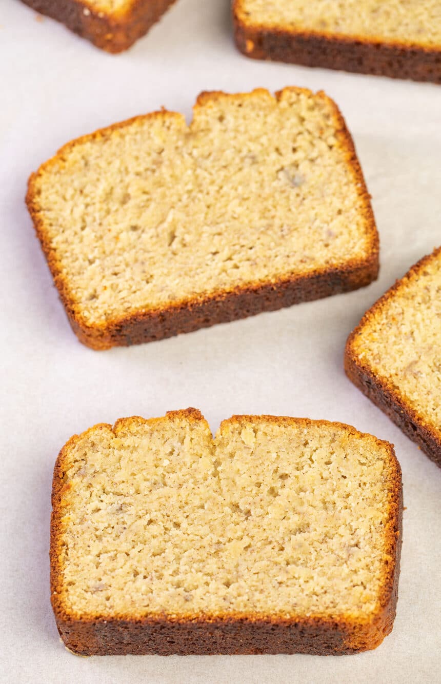 overhead image of 3 slices of light brown banana bread with brown flecks on white paper