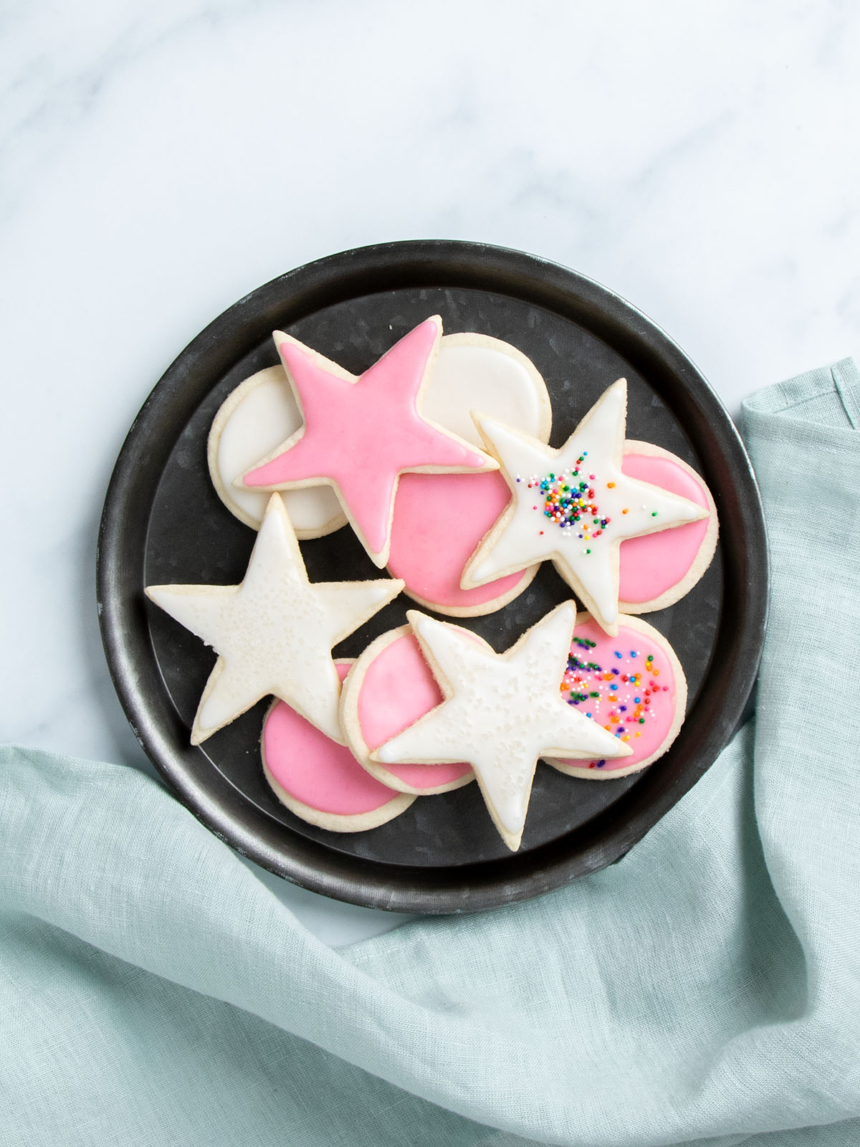 white sugar cookies cut into star and round shapes with white or pink icing on black round plate with blue cloth