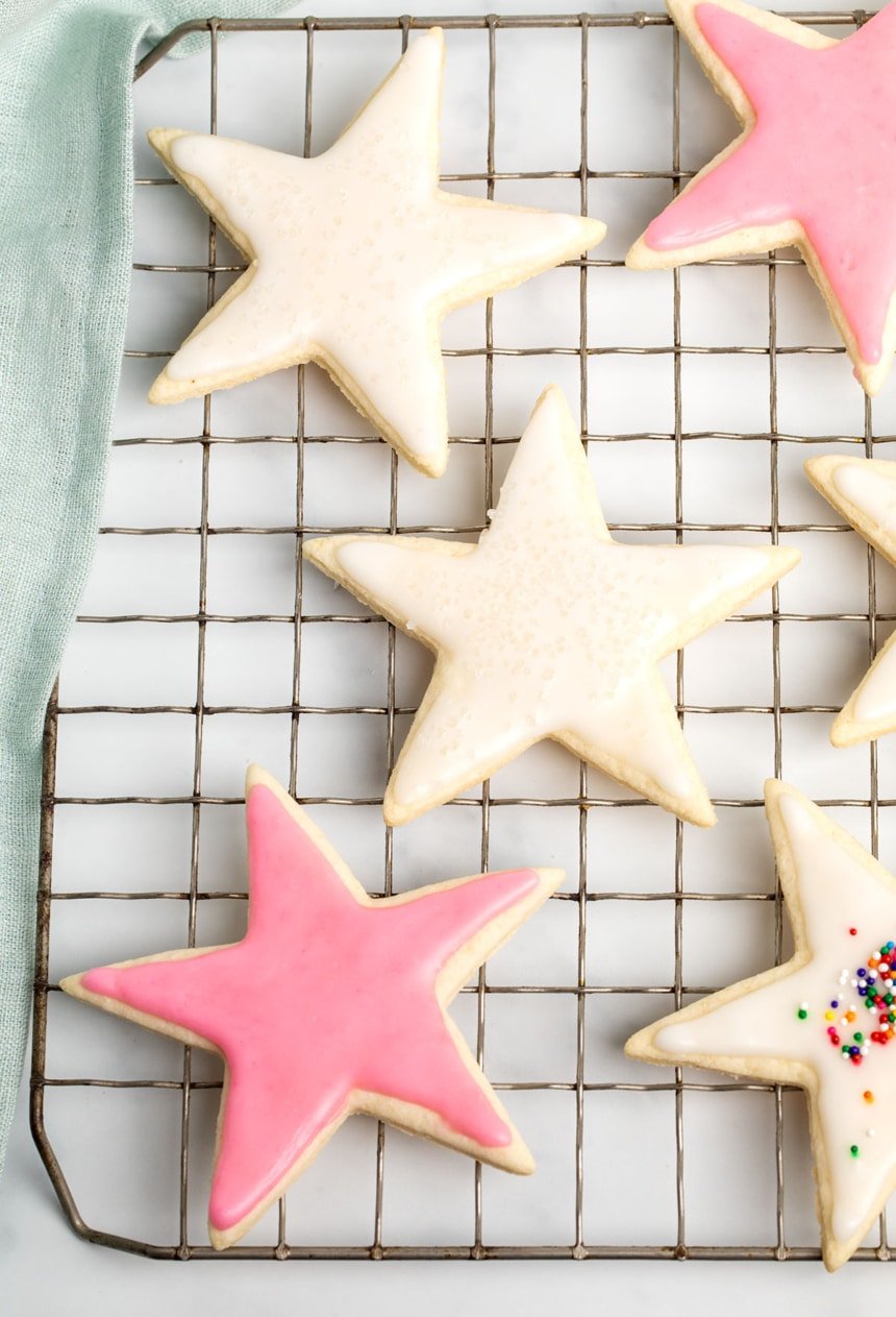 6 star shaped blond sugar cookies with white and pink icing on wire rack with blue cloth on white surface