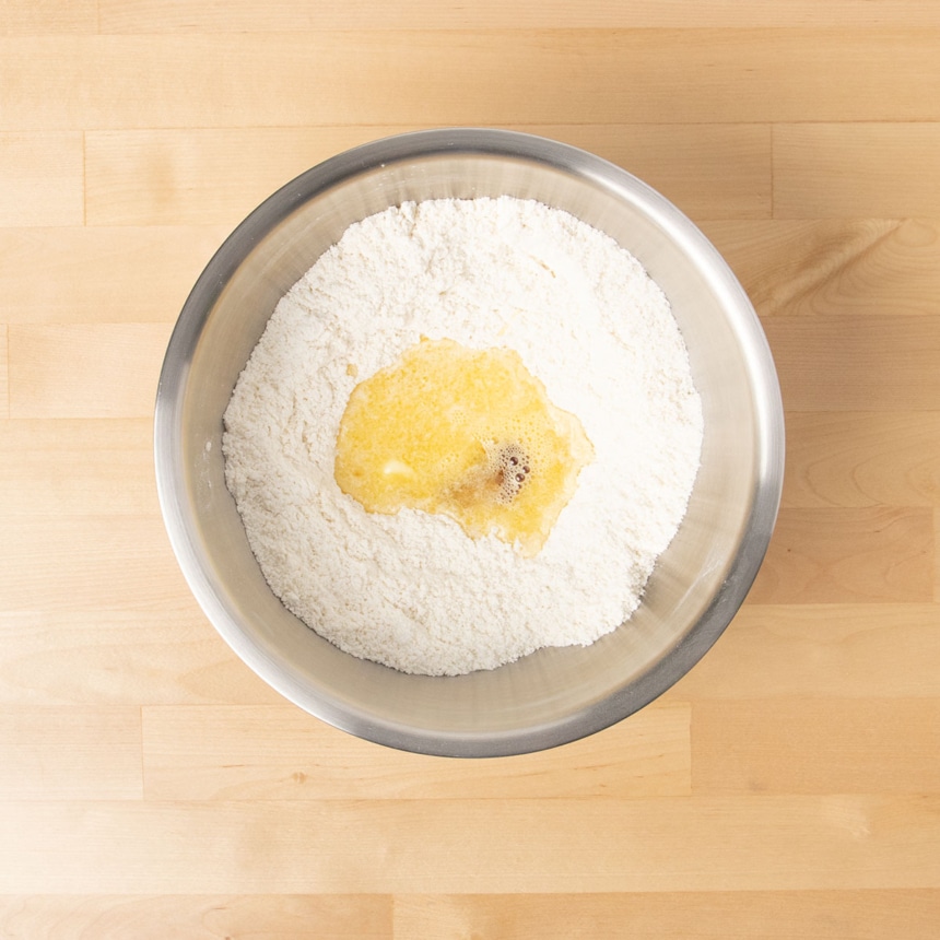 large round metal mixing bowl with whisked dry ingredients and melted butter, beaten egg and vanilla on top