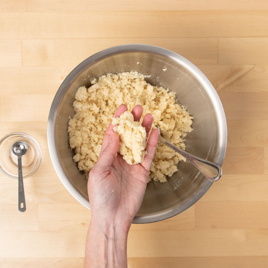 hand squeezing together cookie dough mixture over mixing bowl