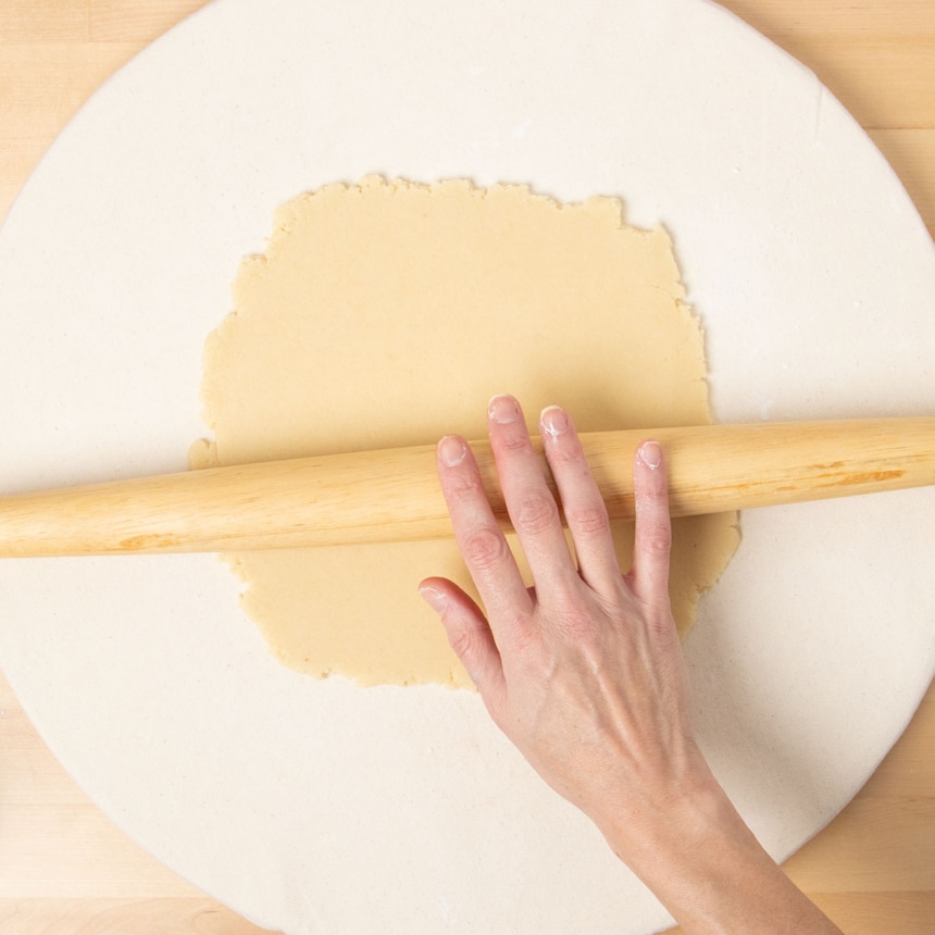 hand pushing french rolling pin over rolled out dough on cloth covered board