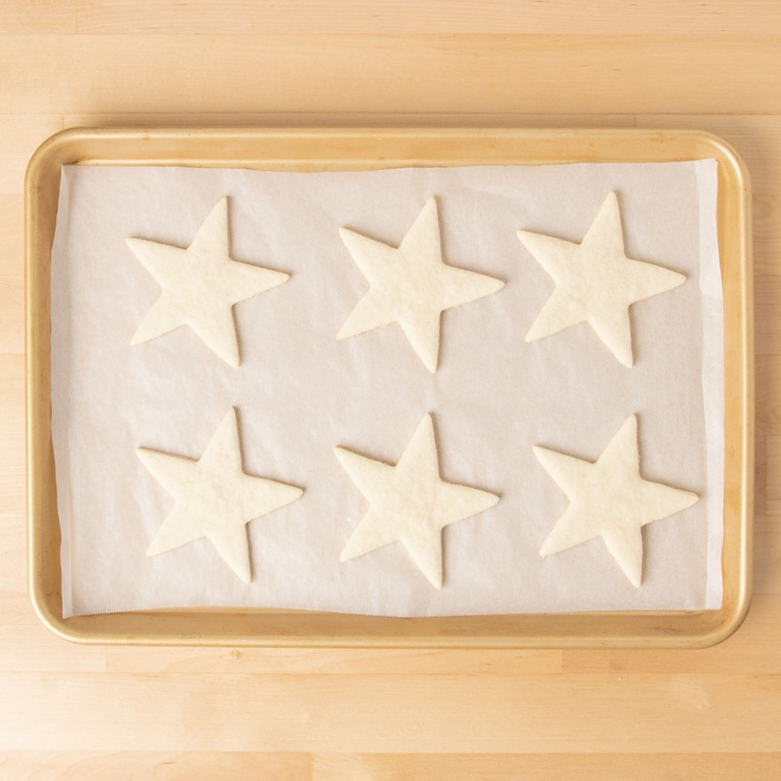 6 baked star shaped sugar cookies on white paper on gold baking tray