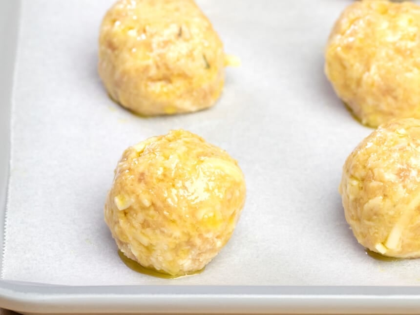 closeup image of 4 raw shaped baked chicken meatballs with olive oil on white paper