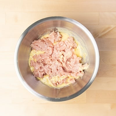 same mixing bowl with crumbled ground chicken on top of yellow liquid