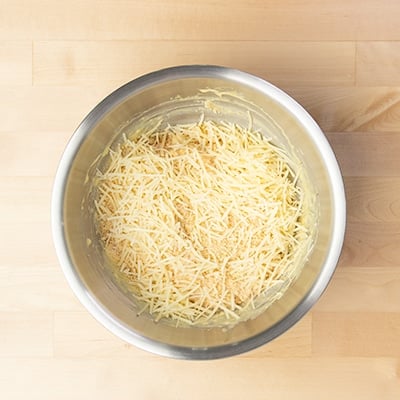 shredded parmesan cheese on top of chicken mixture in mixing bowl