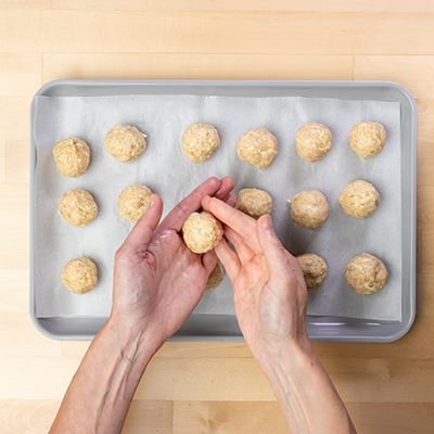 hands shaping raw chicken meatball mixture into rounds with fingers