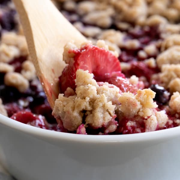 serving spoon in cooked berries and brown crumble topping in white casserole dish