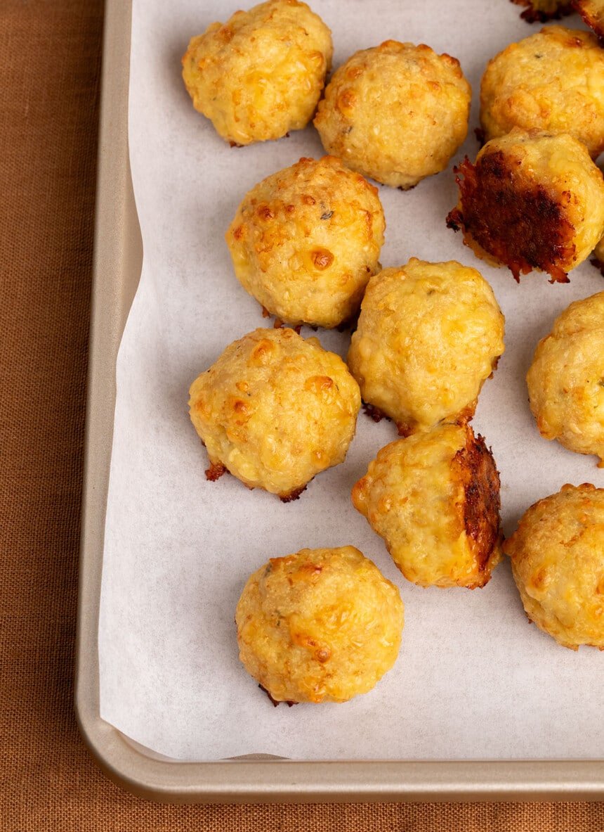 browned baked chicken meatballs on white paper on gold baking sheet with rim