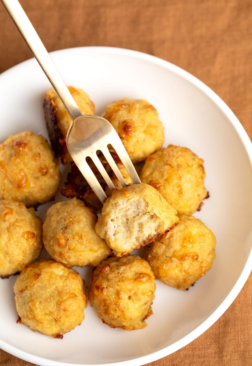 11 baked chicken meatballs in wide flat white bowl with gold fork with one meatball broken in half