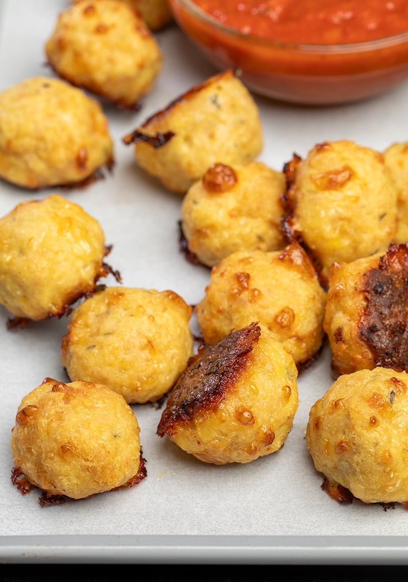 12 baked chicken meatballs on white paper on tray with small bowl of red tomato sauce