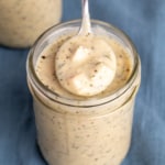 closeup image of spoon in tan gluten free cream of chicken soup with herb flecks in mason jar on blue cloth