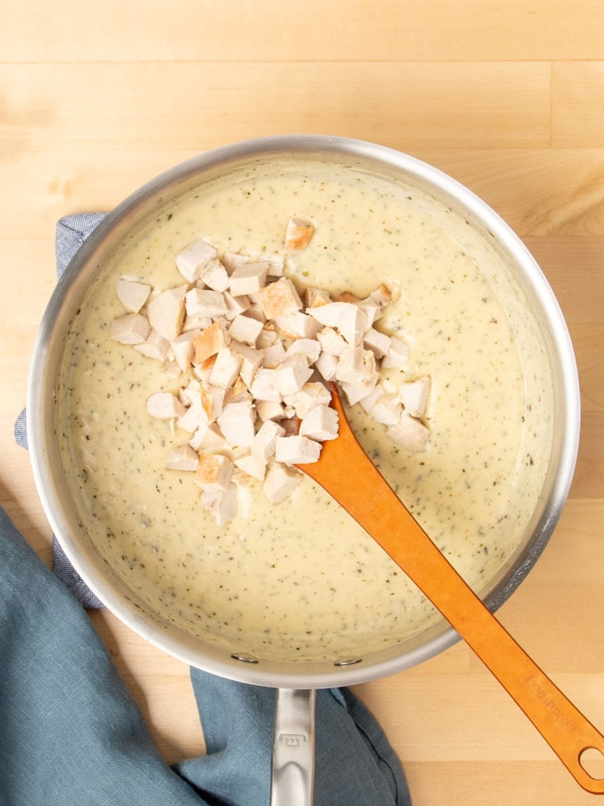 metal saucepan with cream of chicken soup with mixing spoon and chopped cooked chicken on top with blue cloth