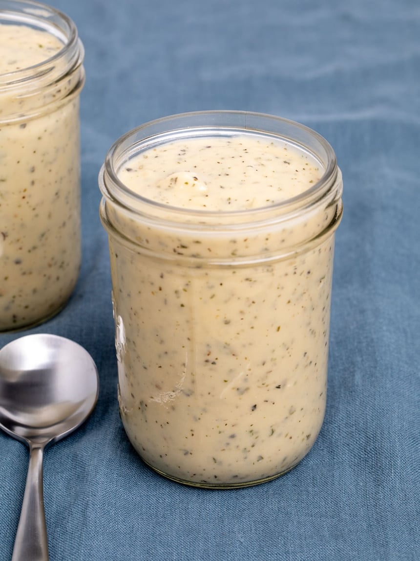 2 glass mason jars with light brown cream of chicken soup with herb flecks on blue cloth and one metal soup spoon on cloth