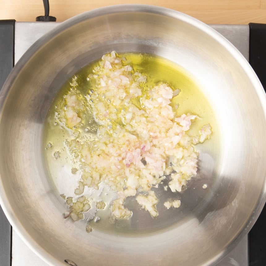 minced shallots simmering in olive oil in round metal saucepan