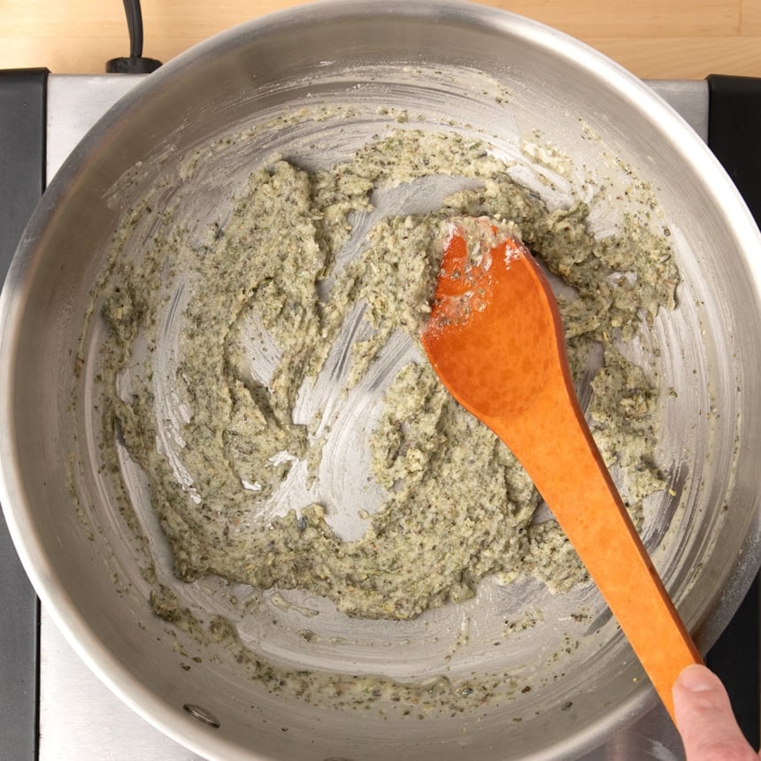 brown mixing spoon stirring light green flecked paste in same saucepan