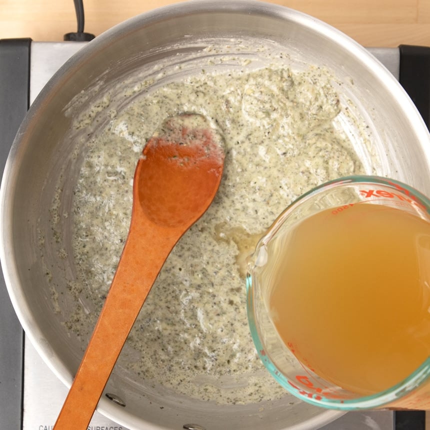 glass measuring cup pouring chicken stock into same saucepan