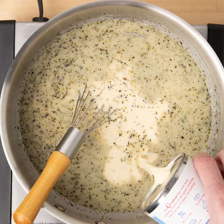 pouring evaporated milk from can into same saucepan with whisk in pan