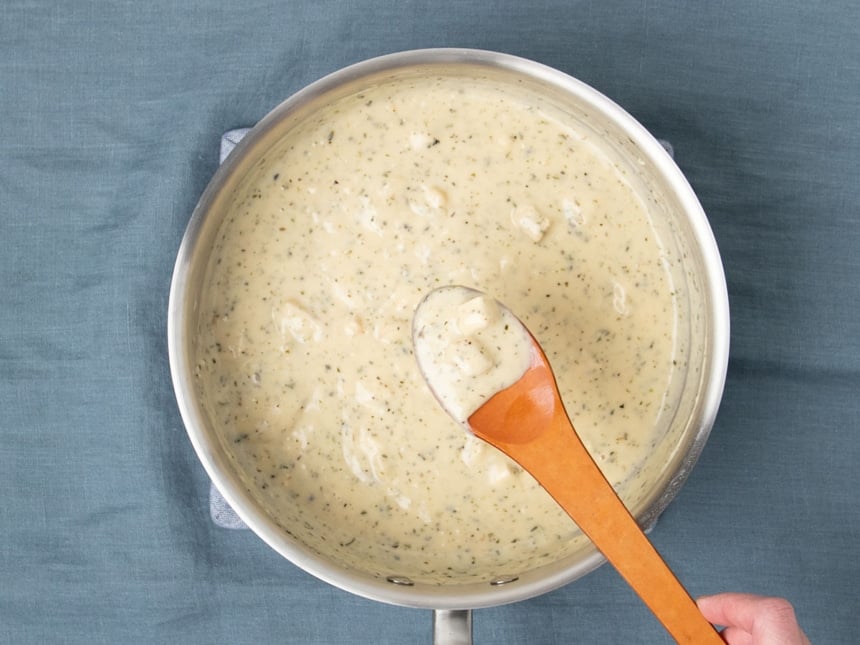 brown mixing spoon with cream of chicken soup over same metal pan on blue cloth