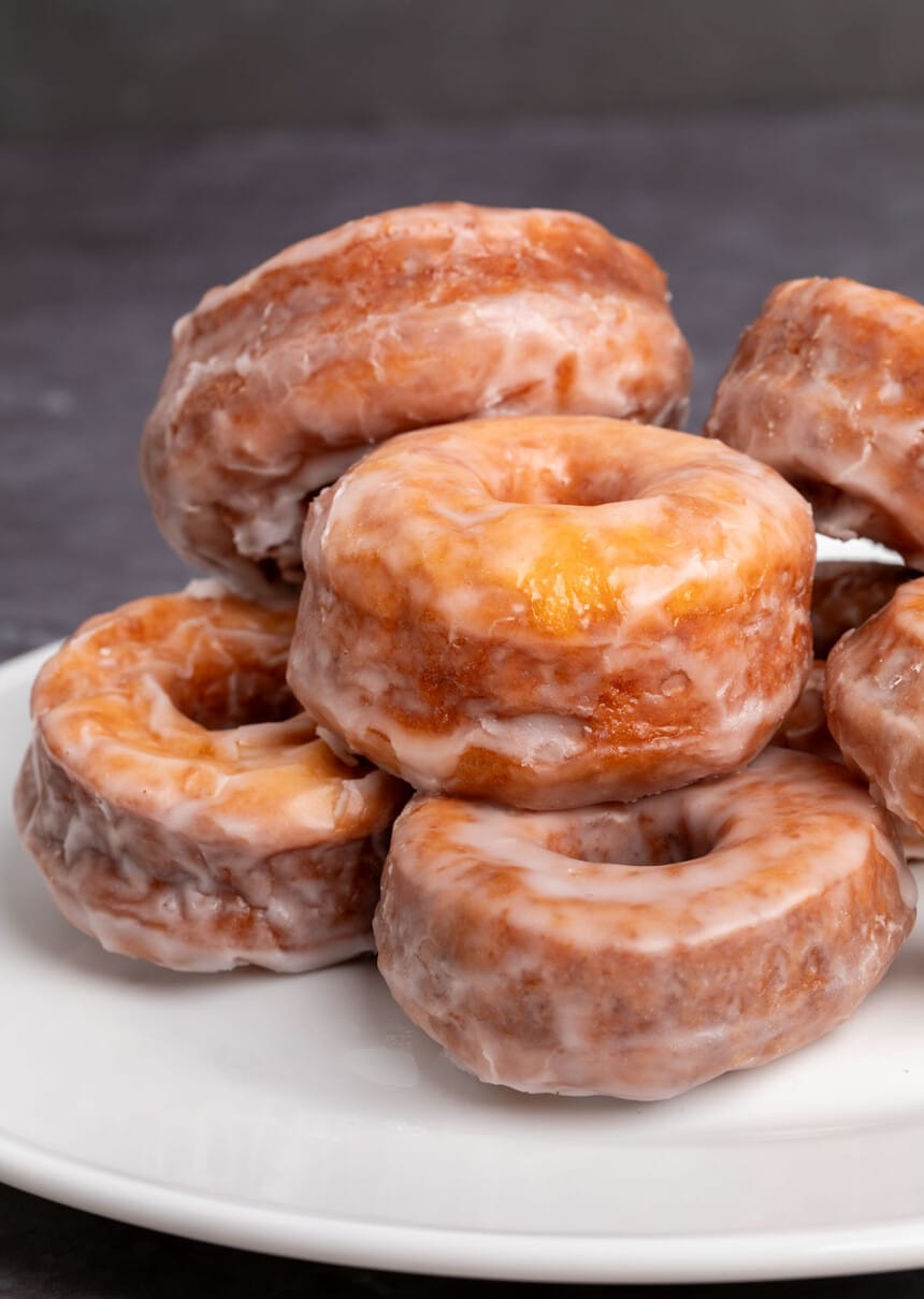 7 brown donuts with white glaze in pile on white platter