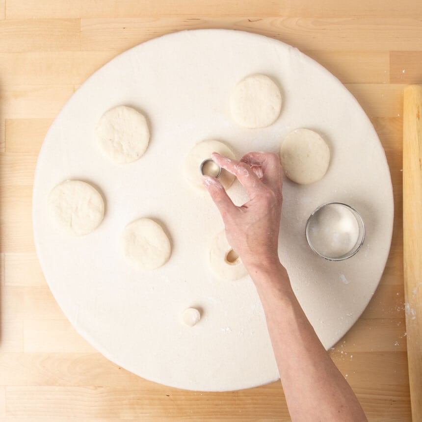 hand cutting out small round from larger round of raw gluten free donut dough