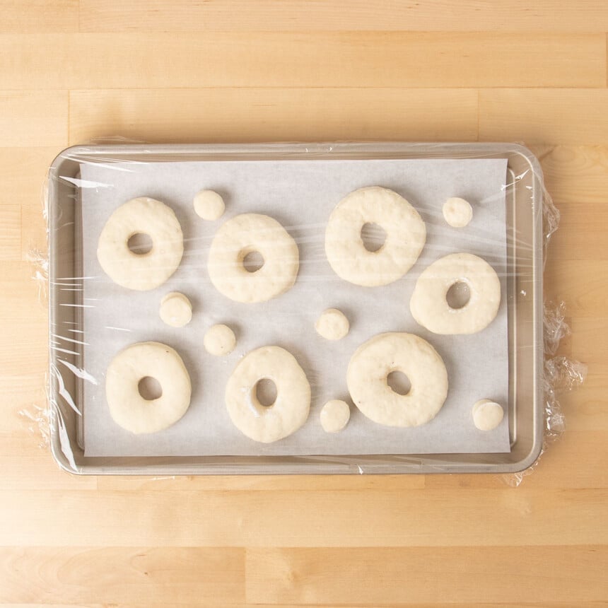 7 raw shaped gluten free donuts and rounds on white paper on tray after rising before being fried