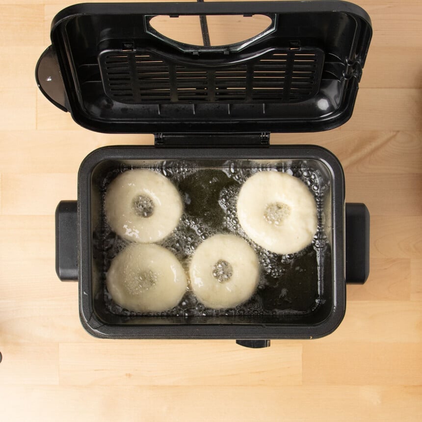 4 raw donuts in frying oil with bubbles