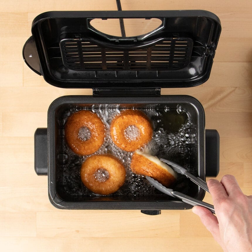 hand using tongs to turn over 4th frying brown donut