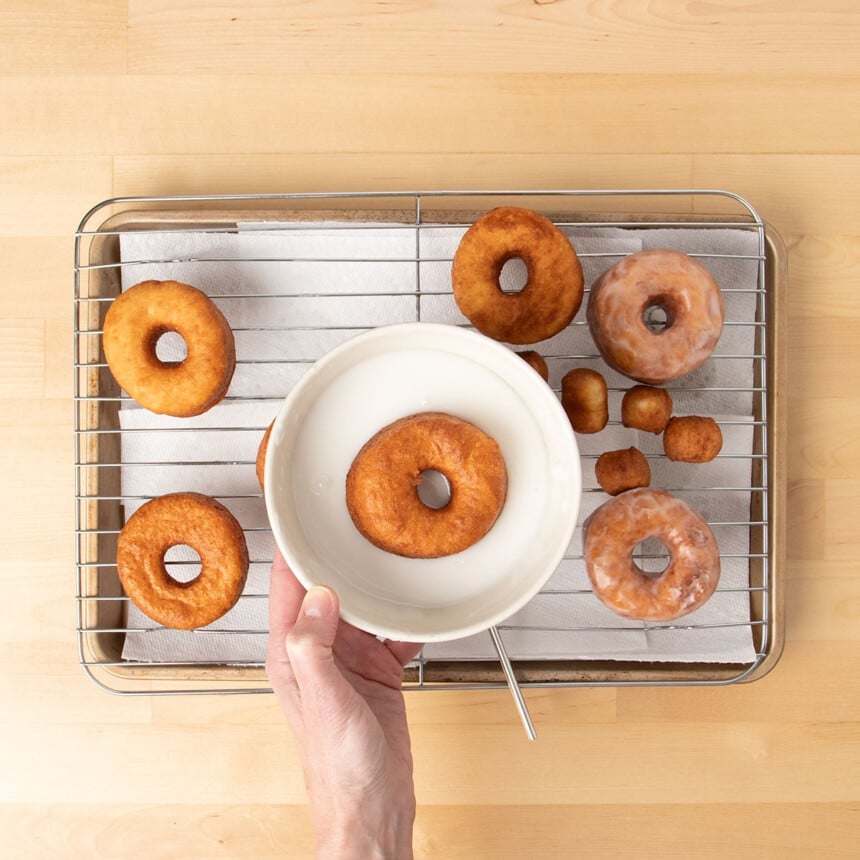 hand holding small white bowl with white liquid glaze and one brown donut inside bowl