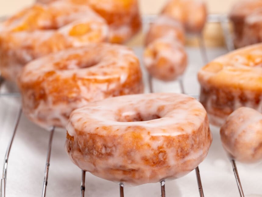 side view of brown donuts with white glaze drying on wire rack