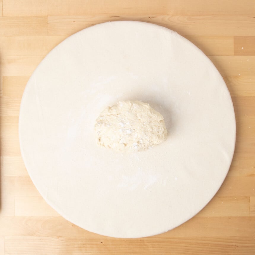 unshaped half raw gluten free donut dough from bucket on white surface with sprinkled flour