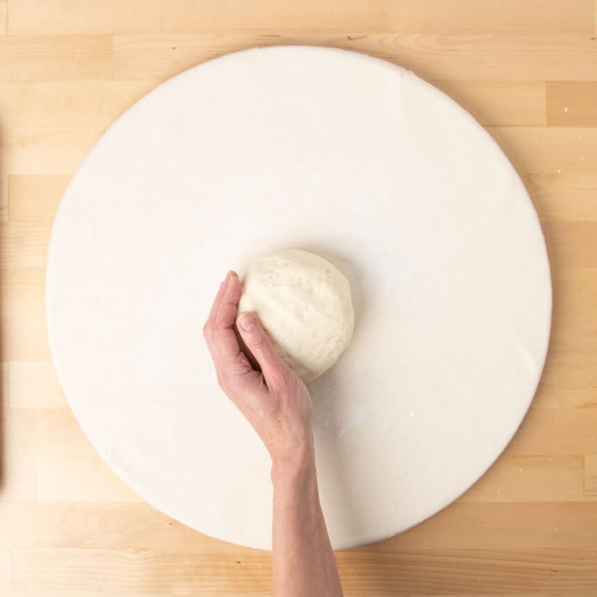 hand shaping raw dough into round on white surface