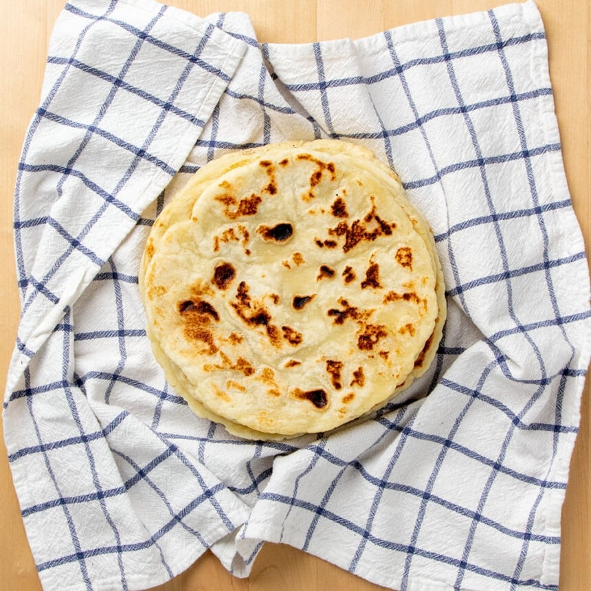 overhead image of stack of round flat bread in white tea towel with blue windowpane stripes