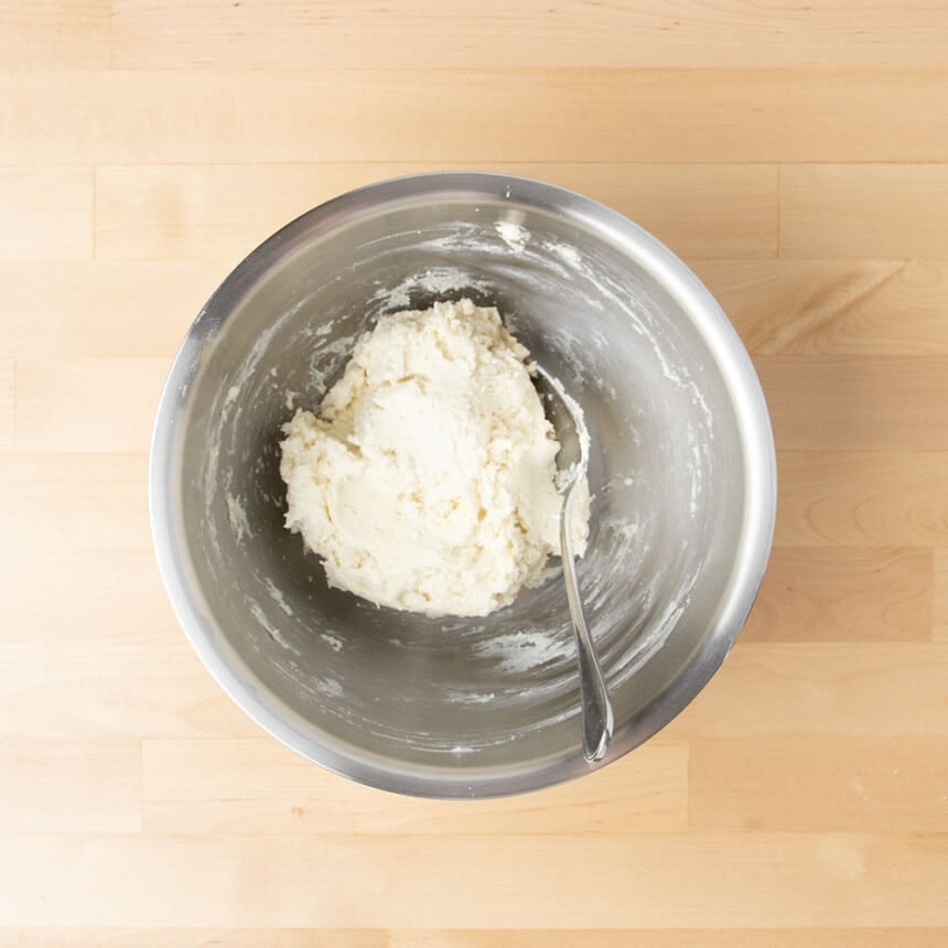 Unshaped raw mixed dough with metal mixing spoon in same round metal mixing bowl