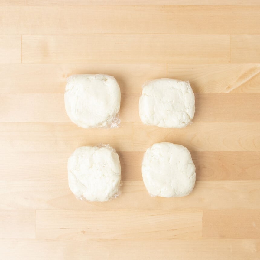 4 light colored small disks of raw dough each wrapped in plastic wrap