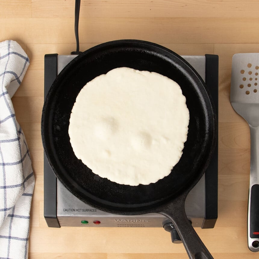 raw round flatbread beginning to form bubbles sitting on black skillet