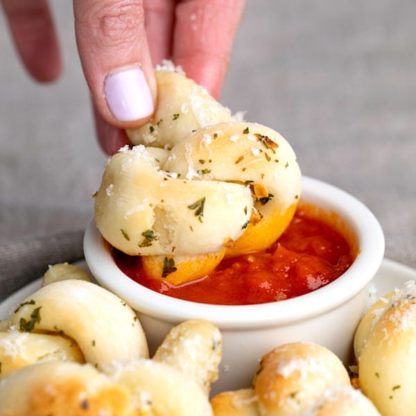 gluten free garlic knots in fingers dipping into tomato sauce in small white ramekin