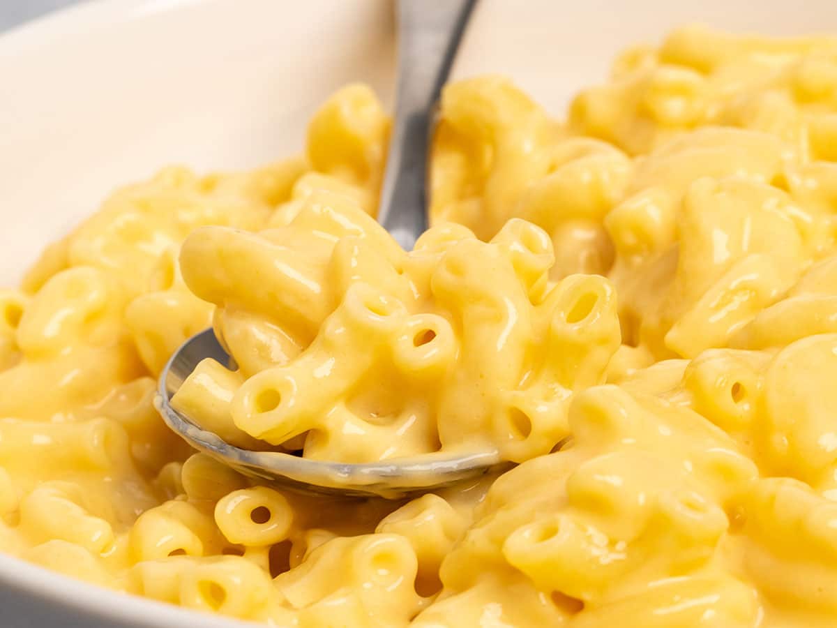 Closeup view of the macaroni in yellow cheese sauce with metal spoon.