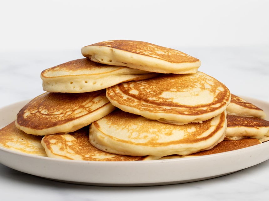 closeup of all 12 light brown cooked pancakes on plate from side angle