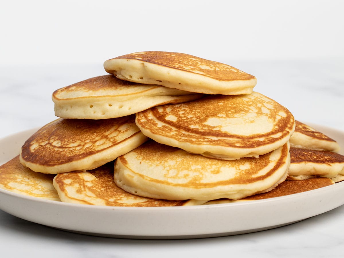 Closeup of all 12 light brown cooked pancakes on plate from side angle.