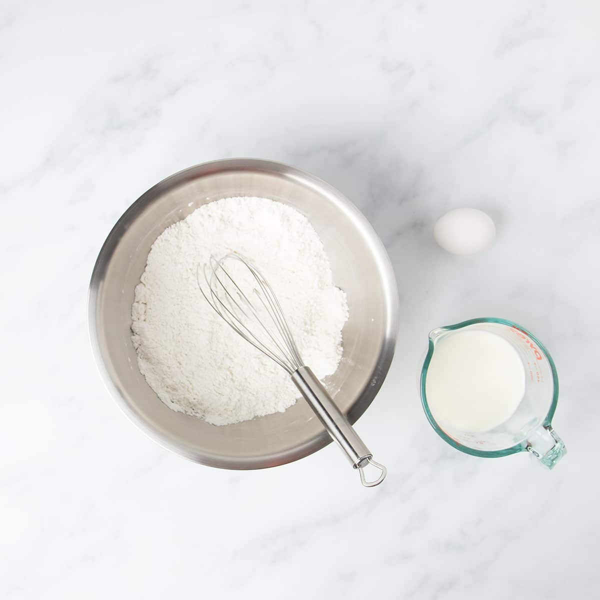 Round metal mixing bowl with white dry ingredients and wire whisk.